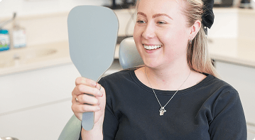 Patient viewing her smile in a mirror during a porcelain veneers consultation